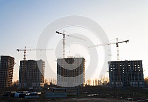 Tower cranes constructing a new residential building at a construction site against blue sky. Renovation program, development,