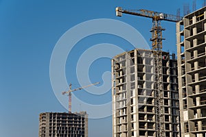 Tower cranes constructing a new residential building at a construction site against blue sky. Renovation program, development,