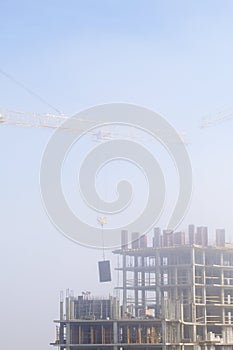 Tower cranes on the construction of a building with a frame of reinforced concrete. Works in the morning mist.