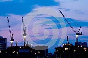 Tower cranes silhouettes and unfinished building construction against night sky