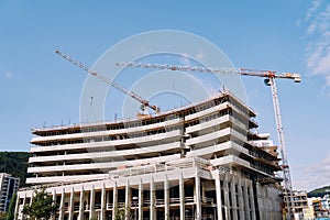 Tower cranes work at the construction site of a multi-storey building against a cloudy sky