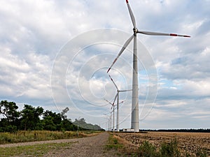 Tower of Eletric power generator wind turbine with rotating blades at sunset against cloudy sky.