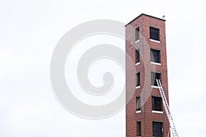 Tower for fire brigade emergency training practise and ladder against red brick facility and blank sky