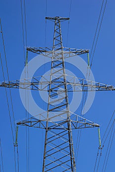 Tower with high-voltage energy transmission wires against the blue sky.