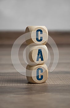 Tower made of cubes and dice with acronym CAC customer acquisition cost on wooden background