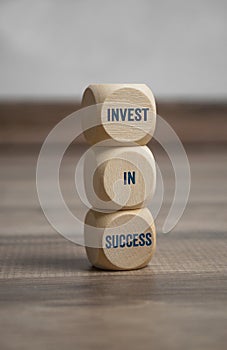 Tower made of cubes and dice showing the message invest in success on wooden background