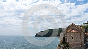 Tower of old fortress, embankment and sea bay in the town of Budva, Montenegro. Round tower with red tiled roof at the wall of the