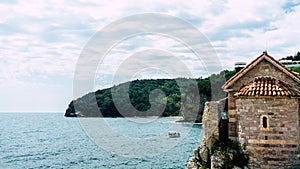 Tower of old fortress, embankment and sea bay in the town of Budva, Montenegro. Round tower with red tiled roof at the wall of the