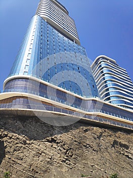 The tower tall high rise office building with glass windows on a rock. view from bottom to blue sky.