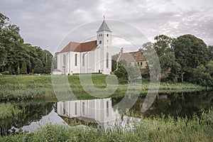 The tower of a white Scandinavian church reflected in a mirror-like lake