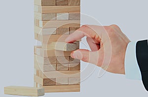 The tower from wooden blocks and man`s hand take one block.