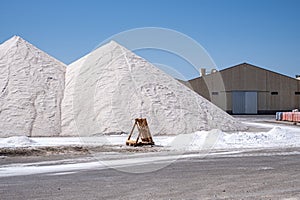 Towering mounds of harvested salt create a minimalist landscape against the backdrop of a stark blue sky.