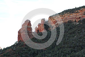 Towering red sandstone rock formation and sheer cliff leading to sloping canyon walls filled with evergreen trees