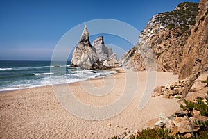 Towering rock cliffs at Praia Da Ursa Beach, Sintra, Portugal. Atlantic ocean waves and sandy beach near famous Cabo Da