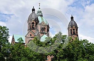 The towers and dome of St Luke`s church in Munich behind trees
