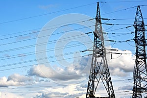 Towers of high voltage electric mainline power line with wires on the background of blue sky with clouds