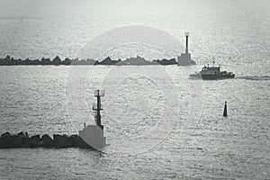 A towing boat swims to the seaport. Breakwaters with lighthouses