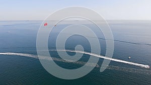 Towing red parachute behind a jetski over the sea along the beach at sunset.