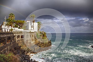 Town city hall over rocks and sea waves under a rainbow