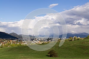 Town, green meadow and hills during sunny and cloudy afternoon.