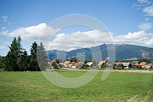 Town, green meadow and hills during sunny and cloudy afternoon.