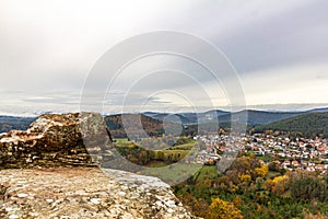 a town nestled in the mountains surrounded by trees and grass with a cloudy sky above it and a few sheep grazing in the foreground