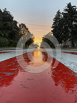 Town sunset with car lights through the road. Reflections on wet white red crosswalk after storm,