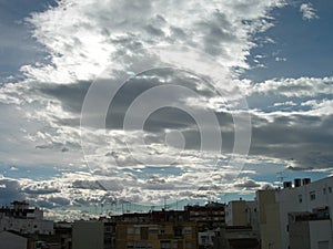 Town under a hidden sun and white clouds travelling.Evening clouds over the town. Ciudad cubierta de nubes photo