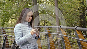 Townswoman is using mobile phone outdoors in autumn day, typing, swiping and tapping photo