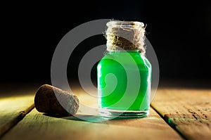 Toxic green drink in magic bottle on black and wooden background. Selective focus