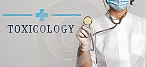 Toxicology - concept of text on gray background. Nearby is a cropped view of doctor with stethoscope