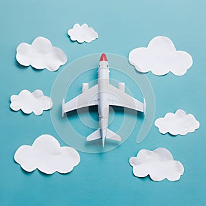 Toy airplane flying through white, cloud like cutouts on a playful and dreamy light blue background