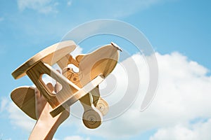 Toy airplane in hand and blue cloudy sky as background.