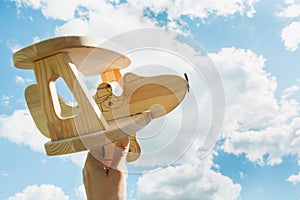 Toy airplane in hand and blue cloudy sky as background.