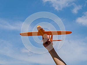 A toy airplane in your hand flies up and forward against a blue sky on a sunny day, a symbol of movement, growth and development,