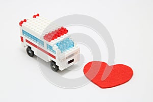 Toy ambulance car and abstract red heart on white background.