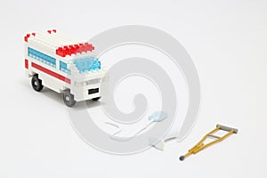 Toy ambulance car, miniature drop, gibbs, and crutch on white background.