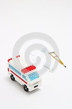 Toy ambulance car, miniature drop, gibbs, and crutch on white background.