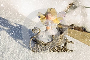 A toy angel sits in a golden sleigh on the snow. Christmas toys.