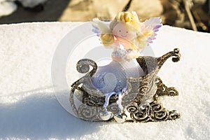 A toy angel sits in a golden sleigh on the snow. Christmas toys.