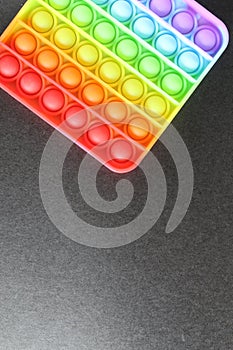 Toy anti-stress popit simlpe dimple rainbow on a black background view from top with space for text copyspace