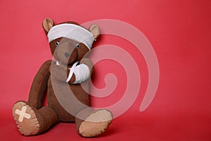 Toy bear with bandages on red background. Space for text