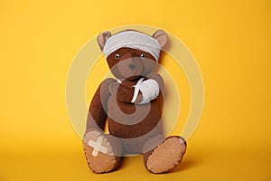 Toy bear with bandages on yellow background