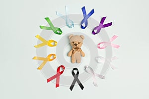 Toy bear with circle of  colorful awareness ribbons on blue background. World cancer day concept, February 4