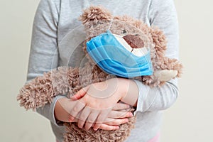Toy bear with protective mask in child hands