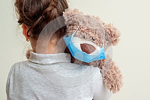 Toy bear with protective mask on child shoulder