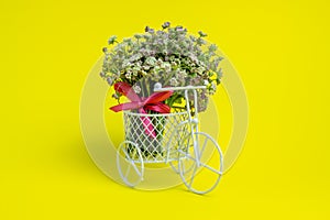 A toy bike carries a flowers. The idea for a postcard. Yellow background. Minimalism