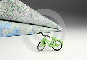 Toy bike and world map guide in airplane shape in background, self-guided travel planning, individual tourism