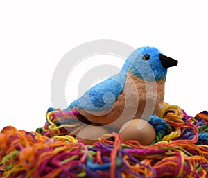 A toy blue and brown bird with a black beak is nesting on two brown eggs
