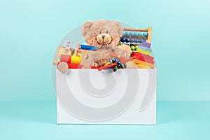 Toy box full of baby kid toys. Container with teddy bear, fluffy and educational wooden toys on light blue background